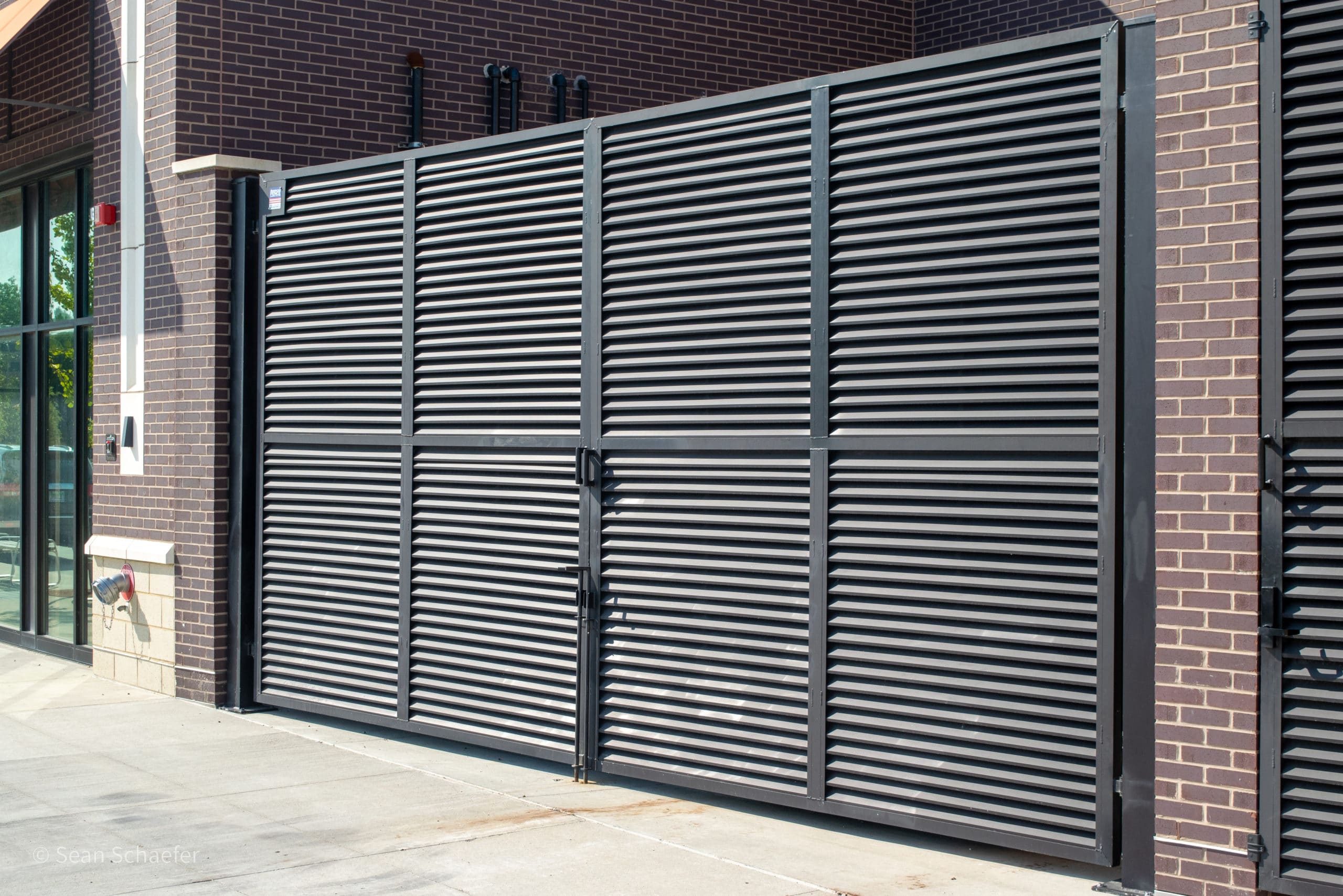 Custom metal (steel AmeriLouver®) louver double-swing dumpster gates and single-swing pedestrian gates with drop rods and panic bars at Woodward Corners by Beaumont